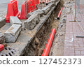 Road repairs, pipe, pile of sand. Red and white plastic barriers blocking the road. 127452373