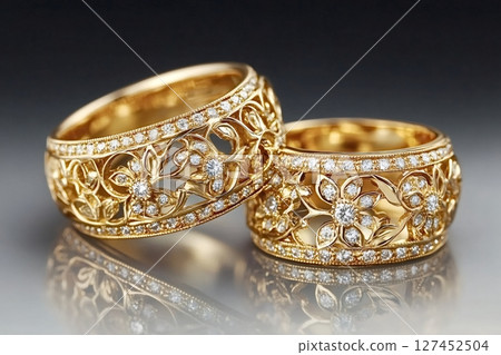 Two golden rings decorated with diamonds and floral motifs reflecting on surface 127452504