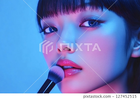 Makeup artist applying pink lipstick with brush in neon lighting 127452515