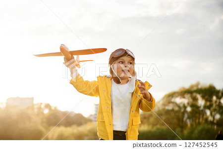 In yellow colored jacket. Little boy is playing with toy plane on the summer field In yellow colored jacket. Little boy is playing with toy plane on the summer field 127452545
