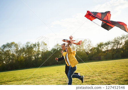Two kids are playing with kite on the summer field Two kids are playing with kite on the summer field 127452546