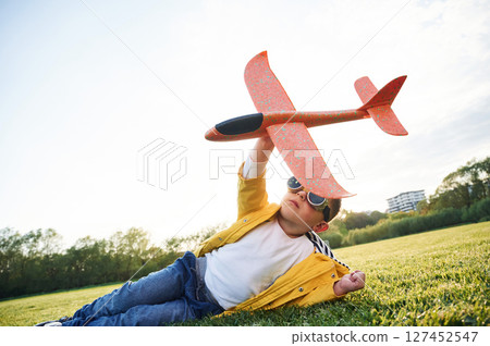 Lying down on ground. Little boy is playing with toy plane on the summer field Lying down on ground. Little boy is playing with toy plane on the summer field 127452547