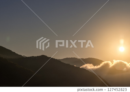 Golden sunlight rises over misty mountain ridges, casting long shadows and illuminating clouds Golden sunlight rises over misty mountain ridges, casting long shadows and illuminating clouds 127452823