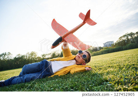 Lying down on ground. Little boy is playing with toy plane on the summer field 127452905