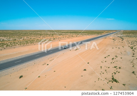 Stretch of highway through barren desert landscape under clear blue sky in remote location Stretch of highway through barren desert landscape under clear blue sky in remote location 127453904