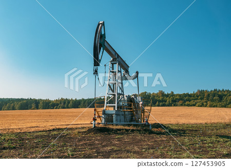 A large oil pump jack operates in an open field, extracting crude oil A large oil pump jack operates in an open field, extracting crude oil 127453905