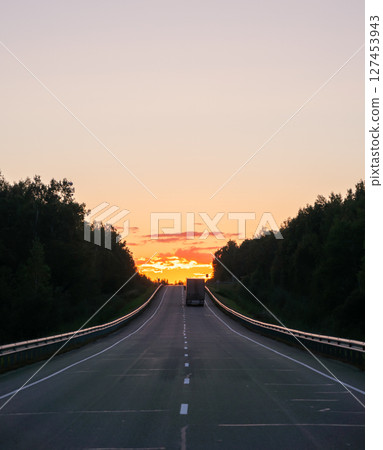 Sunset on an open highway with a lone truck traveling in the distance against a colorful sky 127453943