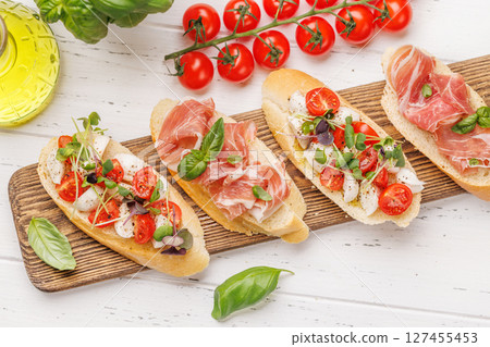 Tasty antipasto toasts featuring classic caprese with mozzarella and tomatoes, and savory prosciutto with herbs 127455453