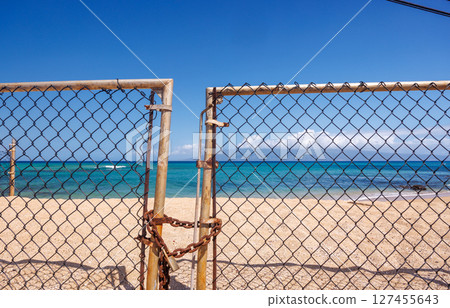 Beach entrance closed with a metal fence and lock in the foreground 127455643