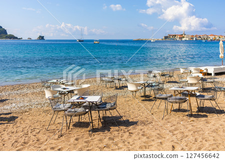 Tables and chairs arranged directly on the beach by the sea. Beachside hospitality, open-air seaside cafe, and coastal tourism ambiance Tables and chairs arranged directly on the beach by the sea. Beachside hospitality, open-air seaside cafe, and coastal tourism ambiance 127456642