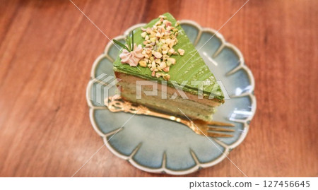 close up of a slice of green pistachio cream cake with layers on a floral plate with copy space on the wooden table  127456645