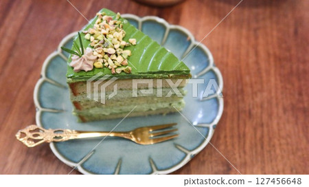 close up of a slice of green pistachio cream cake with layers on a floral plate with copy space on the wooden table  127456648