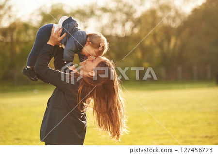 Mother is holding her little daughter in hands on the summer field Mother is holding her little daughter in hands on the summer field 127456723