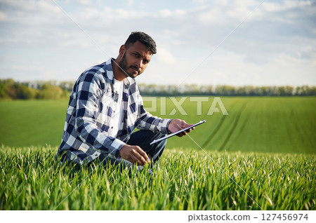 Sitting, checking the wheat, holding notepad. Handsome Indian man is on the agricultural field 127456974