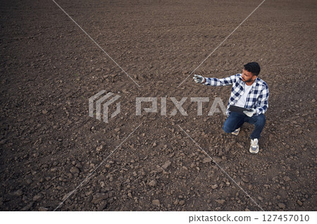 Cultivated agricultural field. Sitting, holding digital tablet. Handsome Indian man 127457010