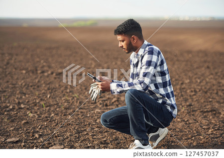 Sitting, holding digital tablet, on the cultivated agricultural field. Handsome Indian man Sitting, holding digital tablet, on the cultivated agricultural field. Handsome Indian man 127457037