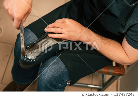 Working with nails on the shoe. Close up view of man that is sitting Working with nails on the shoe. Close up view of man that is sitting 127457242