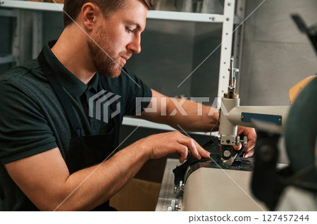 View from the side. Working by sewing machine. Man in black shirt is indoors View from the side. Working by sewing machine. Man in black shirt is indoors 127457244