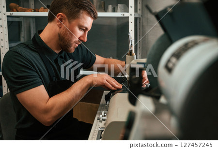 View from the side. Working by sewing machine. Man in black shirt is indoors View from the side. Working by sewing machine. Man in black shirt is indoors 127457245