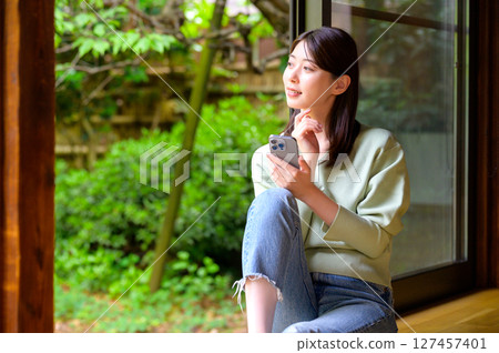 一個輕鬆的午後，一位女士在室內微笑著看著她的智慧型手機 127457401