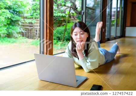 Remote work life of a woman lying face down and operating a laptop in a comfortable space Remote work life of a woman lying face down and operating a laptop in a comfortable space 127457422
