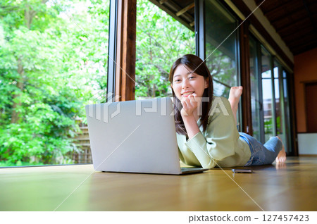 A woman lying on a wooden floor and staring at a laptop computer with a calm expression on her face while working from home A woman lying on a wooden floor and staring at a laptop computer with a calm expression on her face while working from home 127457423