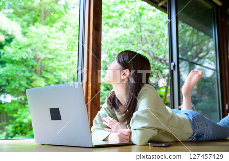 一位女士靠在窗邊，抬頭看著她的筆記型電腦，然後喘口氣，看看周圍的風景。 127457429