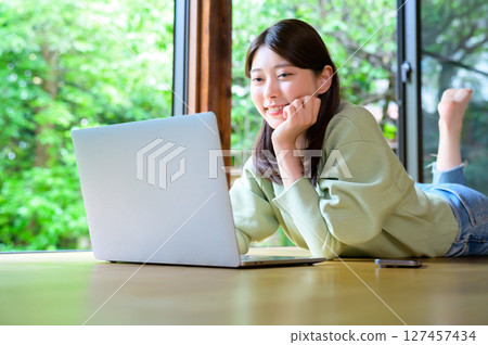 A woman using a laptop in a bright room has a natural smile on her face while concentrating on her work 127457434