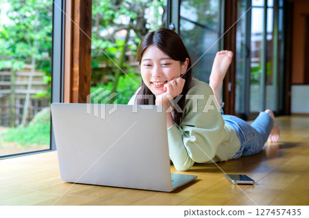 A daily scene of a woman smiling while staring at a computer screen, leaning her chin on her hand, working remotely 127457435