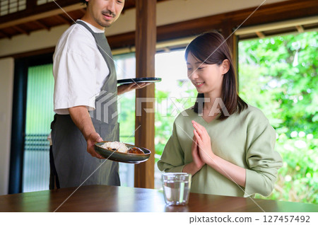 A peaceful moment depicted as a woman clasps her hands together before receiving her food, while a man serving the food looks on. 127457492