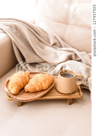 Coffee and croissants served on a wooden tray on a beige couch. Soft focus 127457505