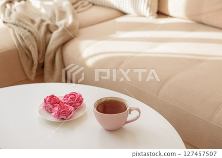 Pink flower marshmallows and tea on a coffee table with a cozy couch. Soft focus 127457507