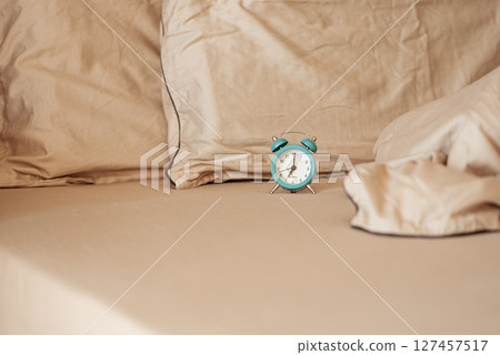 Alarm clock on an unmade bed in the morning light. Alarm clock on an unmade bed in the morning light. 127457517