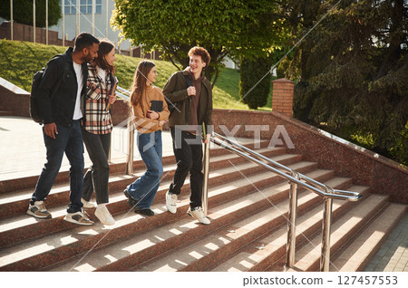 Four young students in casual clothes are together outdoors 127457553