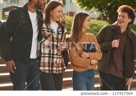 Front view. Four young students in casual clothes are together outdoors Front view. Four young students in casual clothes are together outdoors 127457564