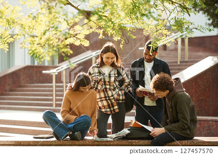 Tree with green leaves. Four young students in casual clothes are together outdoors 127457570