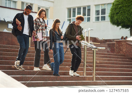 Going down the stairs. Four young students in casual clothes are together outdoors 127457585
