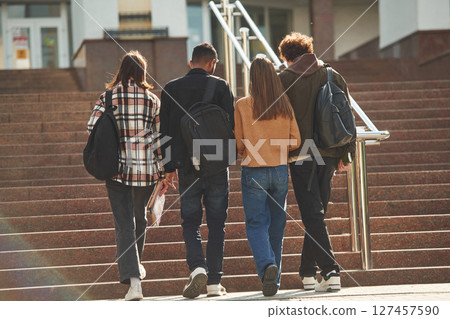 View from back, walking together. Four young students in casual clothes are outdoors View from back, walking together. Four young students in casual clothes are outdoors 127457590