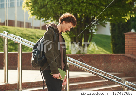 Young student with curly hair is outdoors near university 127457693