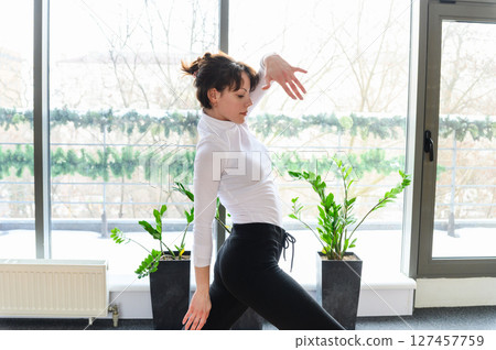 Woman in graceful dance stretch pose near panoramic window. 127457759