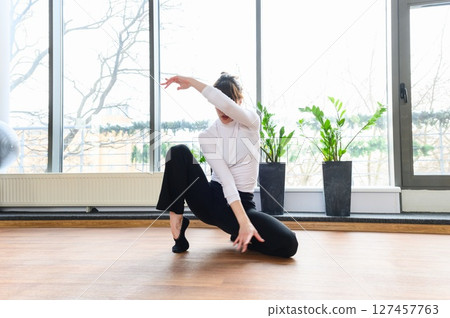 Woman in modern dance floor pose near large window. 127457763