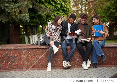 Four young students in casual clothes are together outdoors 127457879