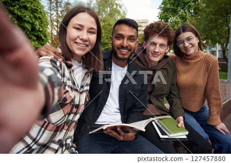 Making selfie. Four young students in casual clothes are together outdoors 127457880
