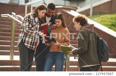 Hanging out after lessons. Four young students in casual clothes are together outdoors Hanging out after lessons. Four young students in casual clothes are together outdoors 127457897