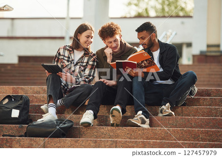 Students are sitting on the stairs. Young people in casual clothes are together outdoors Students are sitting on the stairs. Young people in casual clothes are together outdoors 127457979