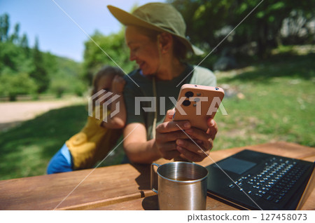 Woman Working Remotely at Outdoor Destination with Child and Digital Devices 127458073