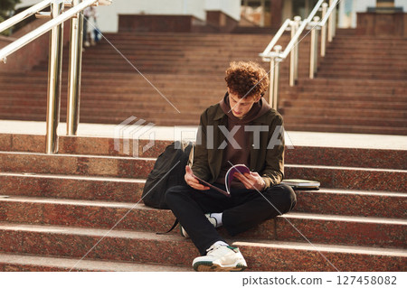 Notepad in hands. Young student with curly hair is outdoors near university Notepad in hands. Young student with curly hair is outdoors near university 127458082
