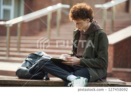 With backpack. Young student with curly hair is outdoors near university 127458092