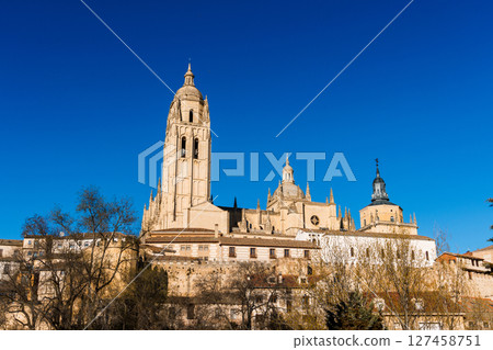 The Segovia Cathedral towers over the city under a clear blue sky near the Guadarrama mountains. The Segovia Cathedral towers over the city under a clear blue sky near the Guadarrama mountains. 127458751