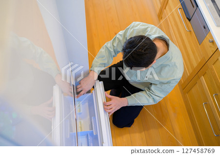 Japanese man in work clothes inspecting a refrigerator Japanese man in work clothes inspecting a refrigerator 127458769